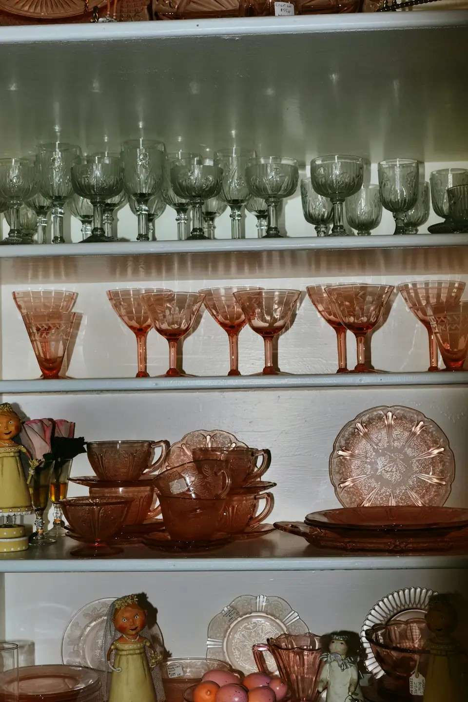 Shelves of vintage stemware, pink depression glass coupes and plates in an antique shop