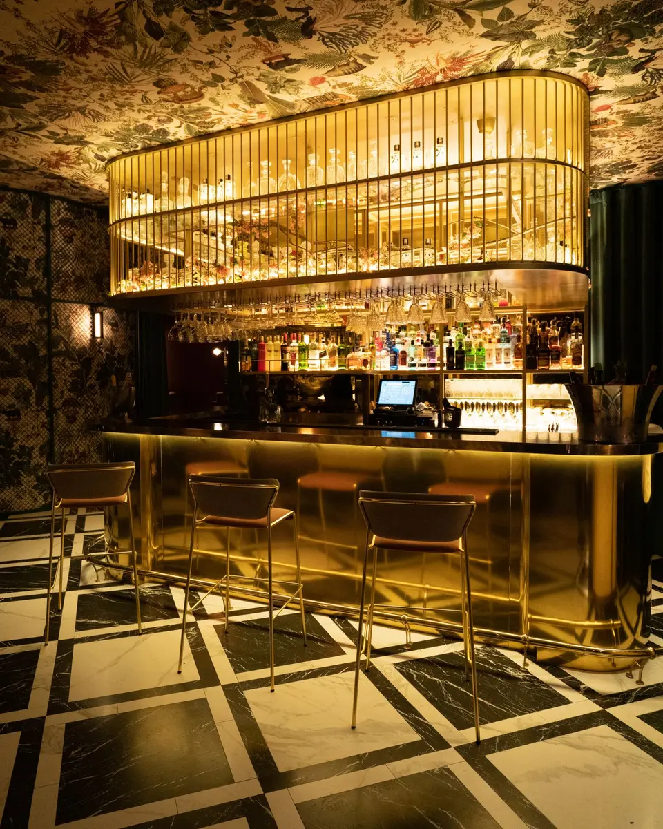 An Art Deco style bar with a glowing golden glass canopy, brass bar counter and geometric tiled floor