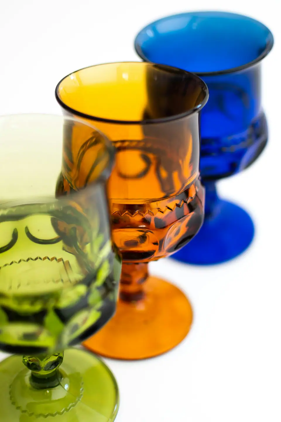 Cobalt blue, amber and green pressed glass goblets side by side on a white background