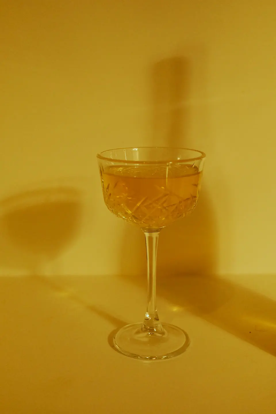 An etched crystal coupe holding an amber cocktail against a warm golden backdrop