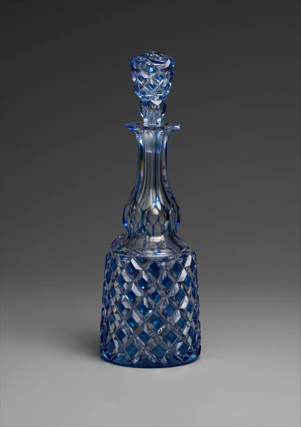 A blue cut-to-clear glass decanter made by the Brooklyn Flint Glass Company in 1850 to 1855, with a diamond-cut body and a matching faceted stopper