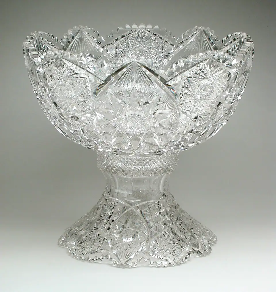 A deeply cut clear glass punch bowl with a scalloped rim on a matching cut glass stand, made by the Meriden Cut Glass Company around 1895