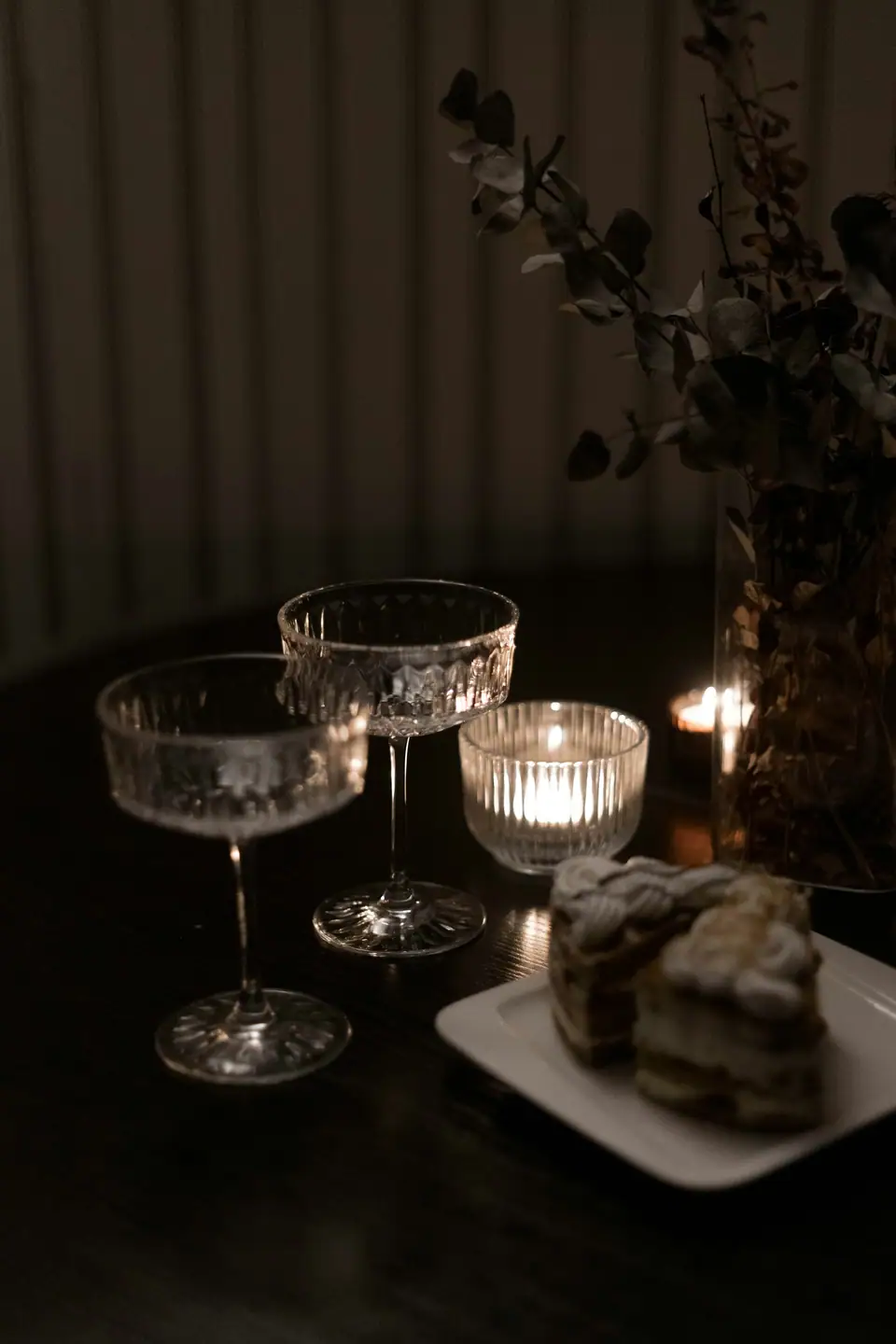 Two etched crystal coupes beside lit candles on a dark table