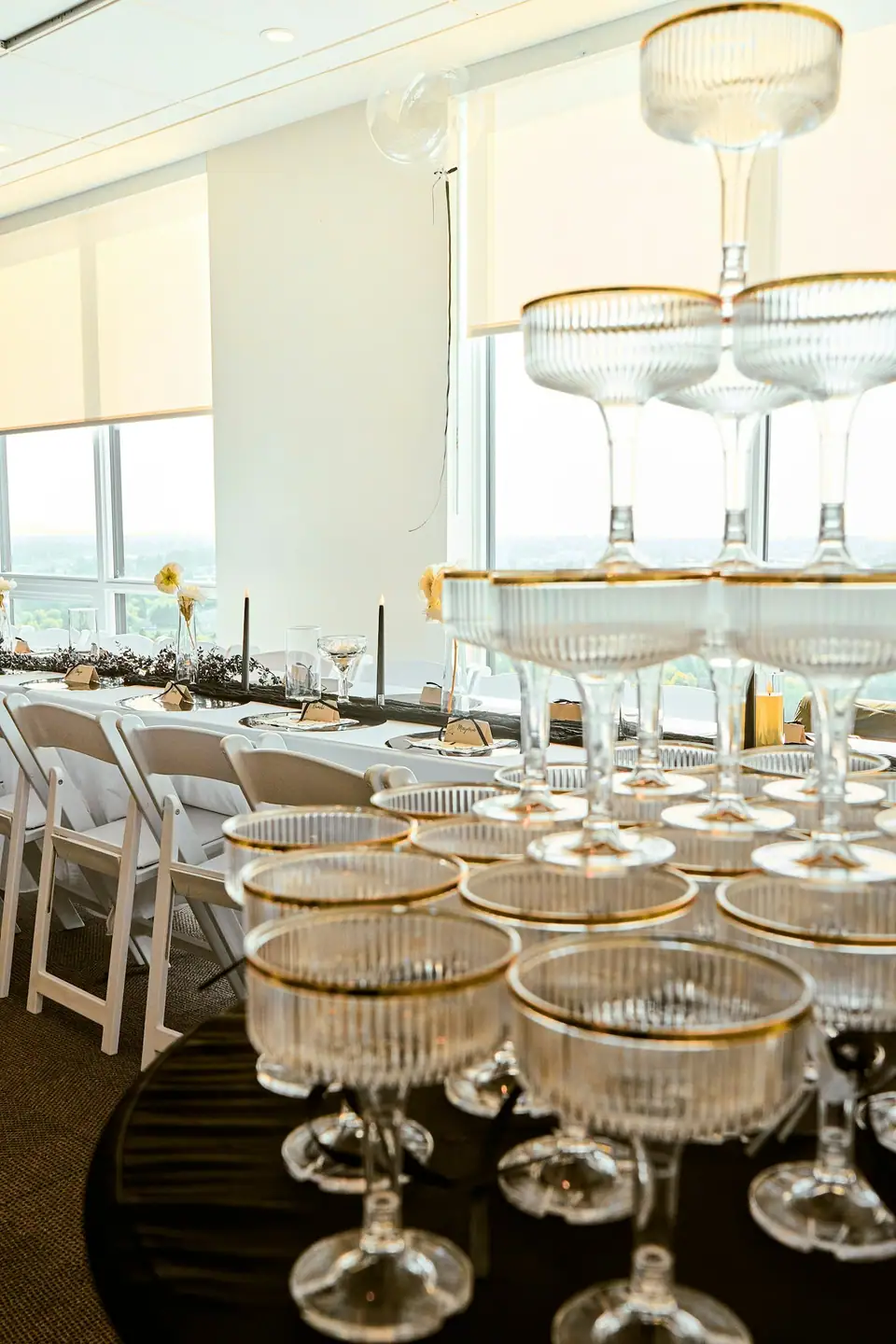 A tower of ribbed champagne coupes with gilded gold rims set up in a bright event room