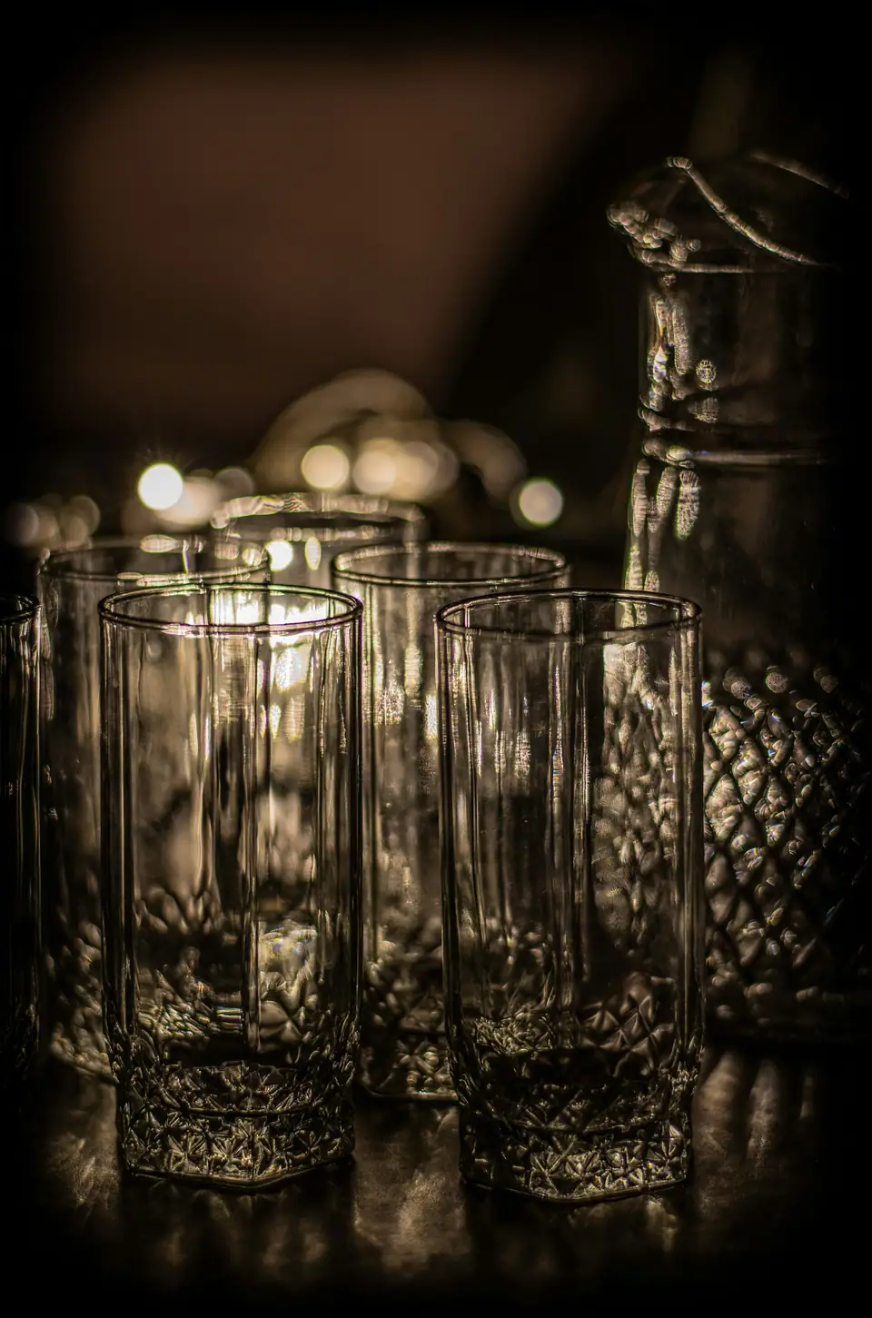 Tall cut glass tumblers grouped on a dark bar in low light