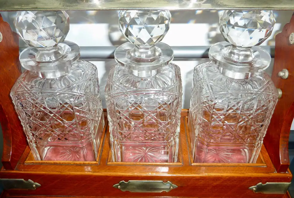 Three hobnail cut glass decanters with faceted stoppers in an oak tantalus