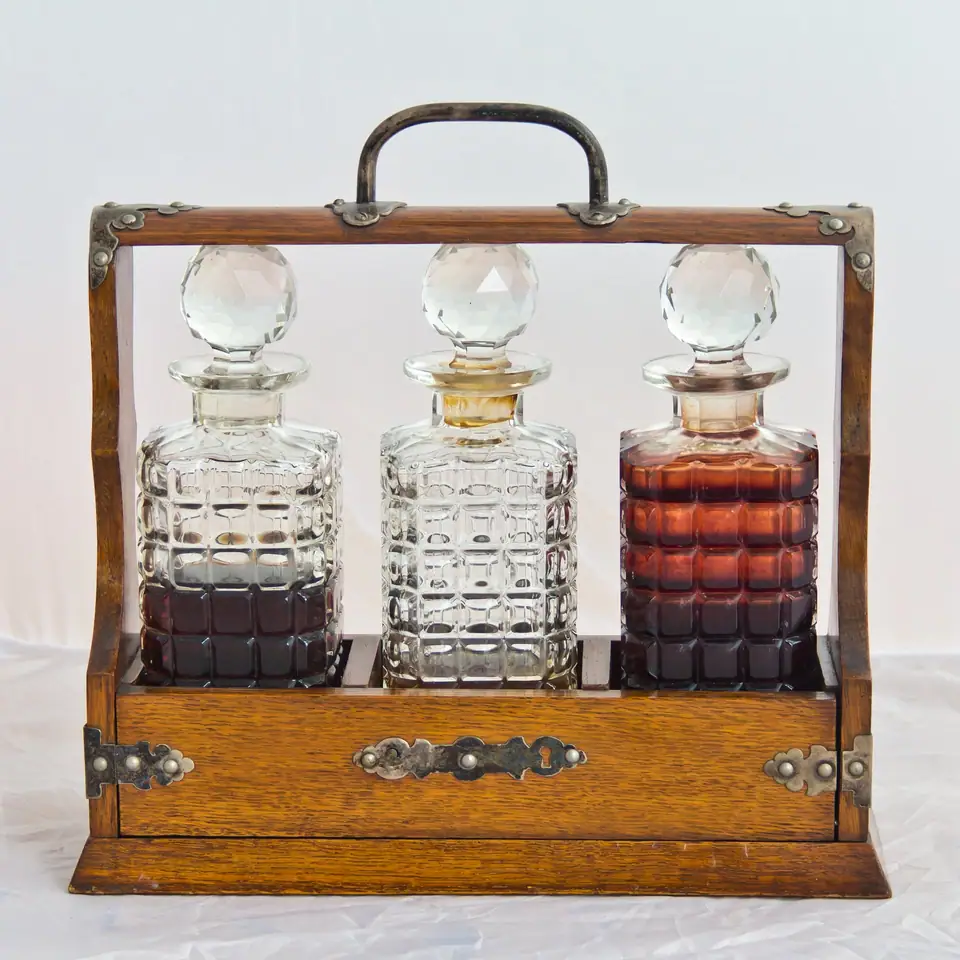 An oak tantalus holding three square cut glass decanters behind a locked bar