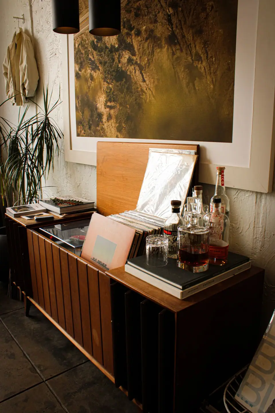 A mid-century wooden sideboard used as a home bar, with a record collection, a glass decanter and a tumbler on top