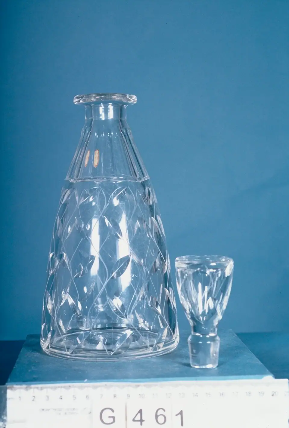 A cut crystal decanter and stopper by John Walsh Walsh, designed by W. Clyne Farquharson, on a blue museum backdrop
