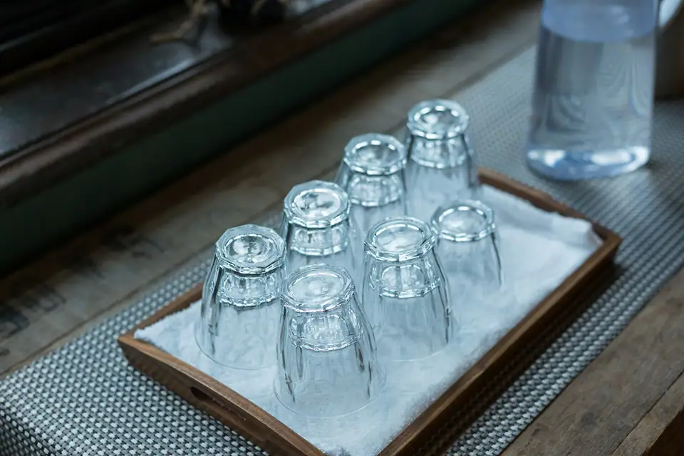 Cut glass tumblers drying upside down on a white towel laid in a wooden tray