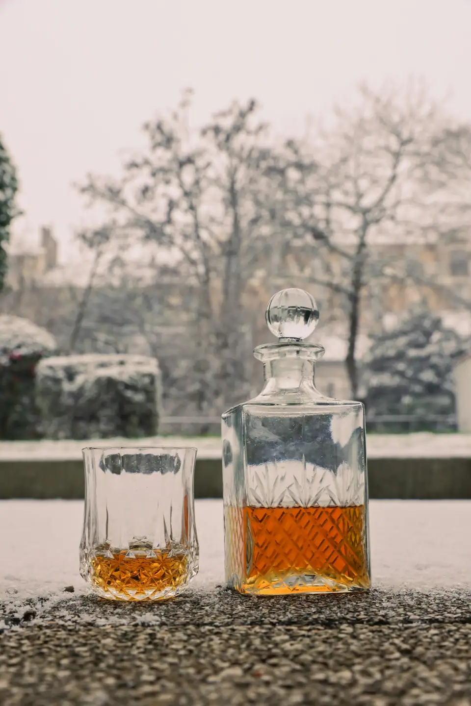 A cut crystal decanter of whisky and a matching glass on a ledge against a pale wintry window view
